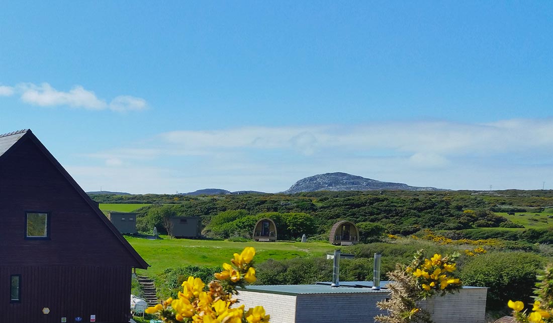 Panoramic view Glamping Pod site from a distance with Holyhead Mountain (Mynydd Tŵr) in the background