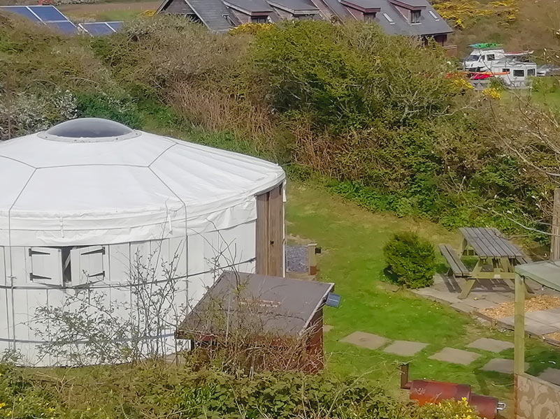 Traditional White glamping yurt with the front doors open in the sunshine and green bracken at its side