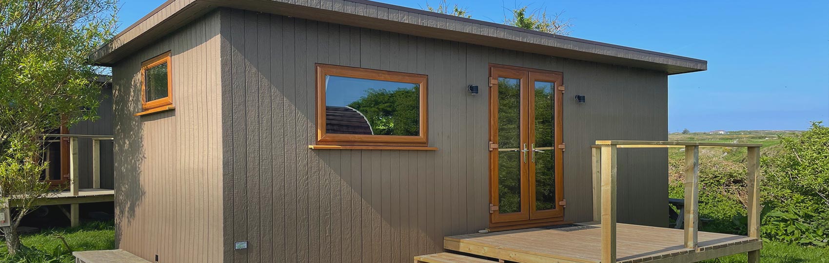 Eco Den with front doors open on the grass with Anglesey Outdoors Main Centre in the background