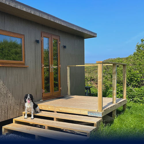 Eco Den front door and balcony with a cocker spaniel sitting on the steps